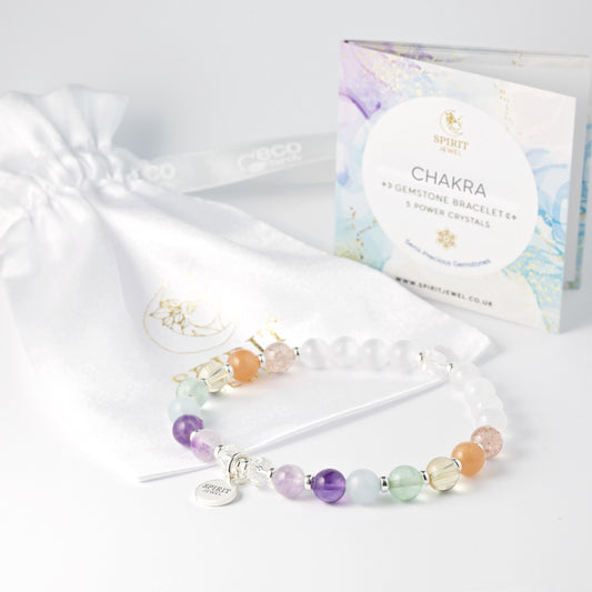 a bracelet with colorful beads and a small charm, placed next to a white gift bag and a box of chakra bracelets.