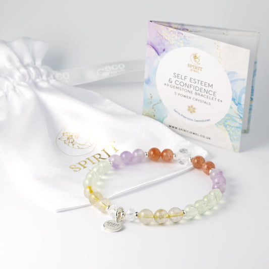 a bracelet with colorful gemstones and a white drawstring bag with a gold logo, along with a package of the bracelet and a booklet.