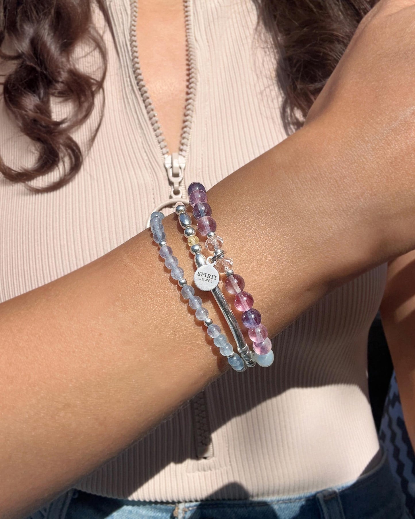 A person wearing a beige top and bracelets on their wrist.