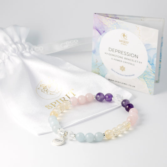 a bracelet with various colored gemstones, including blue, pink, yellow, and clear stones, as well as a white drawstring bag and a box of depression gemstones.