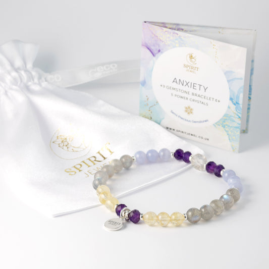 a bracelet with various colored stones, including blue, purple, and yellow, as well as a white drawstring bag with a gold logo and text.