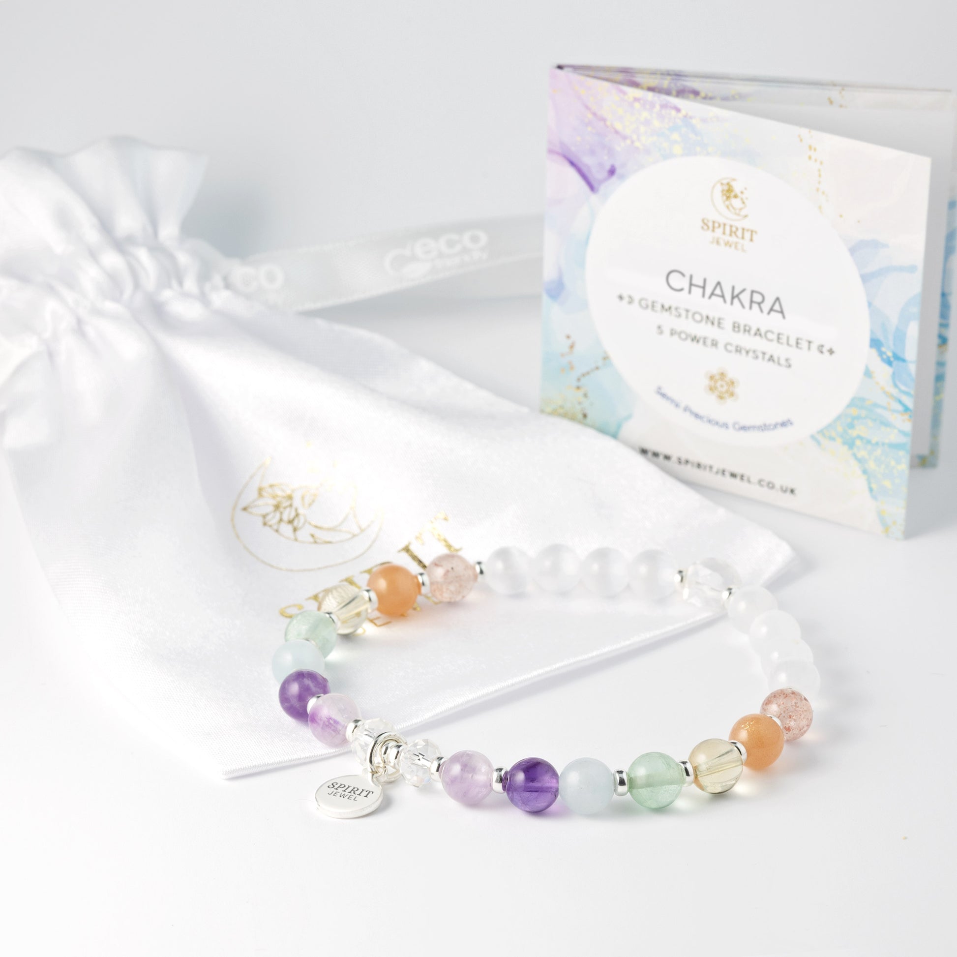 a bracelet with colorful beads and a small charm, placed next to a white gift bag and a box of chakra bracelets.