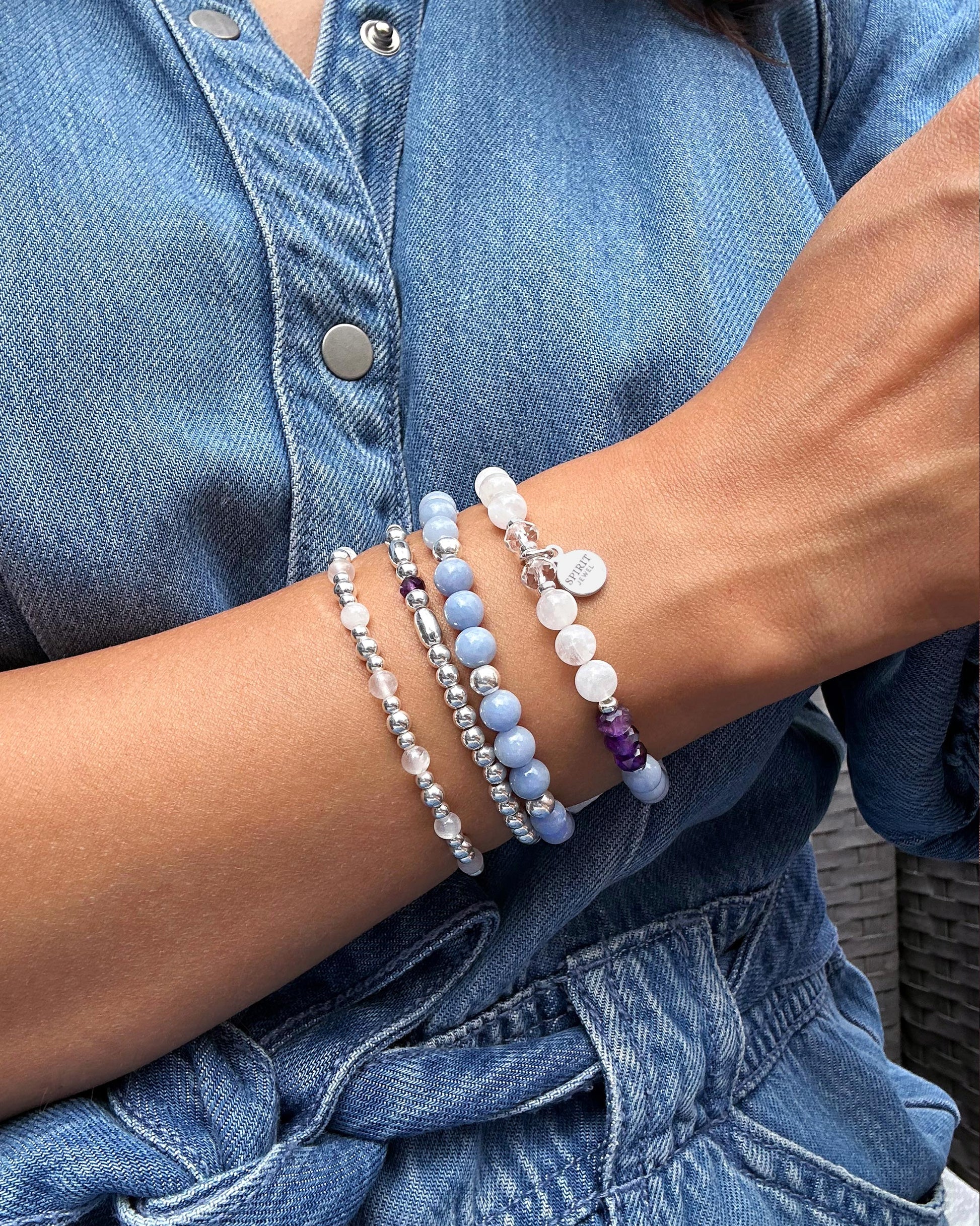 A person wearing a denim shirt and jeans is wearing multiple bracelets on their wrist.