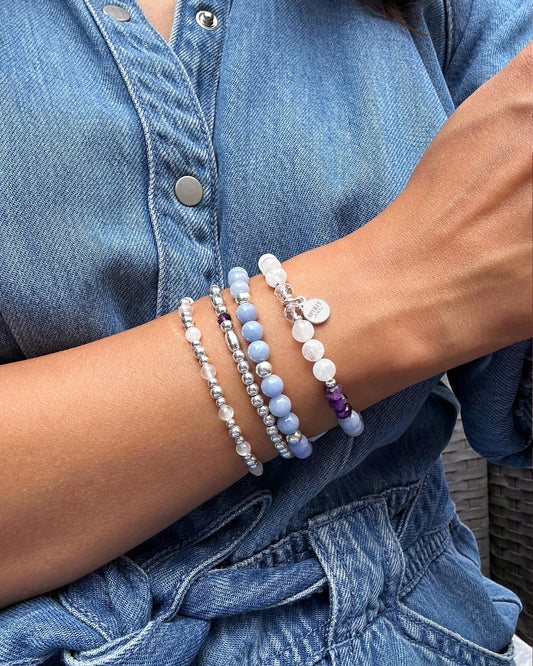 A person wearing a denim shirt and jeans is wearing multiple bracelets on their wrist.