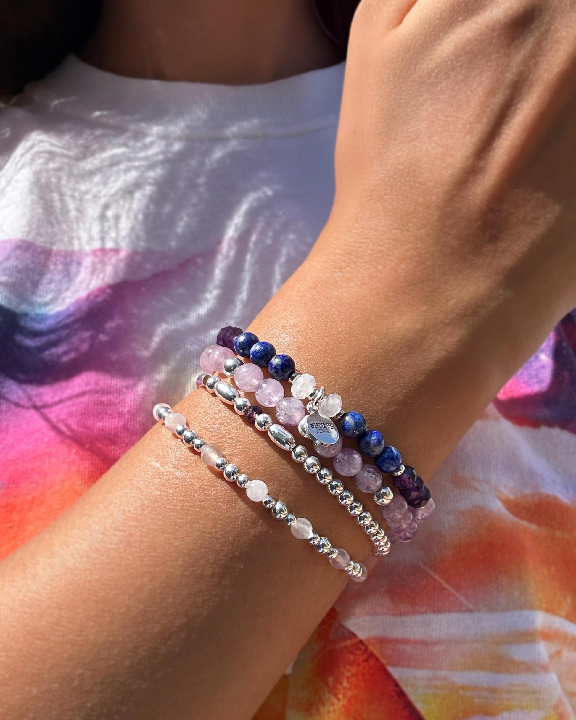 A person's wrist adorned with a stack of colorful beaded bracelets, including silver, blue, and purple stones.