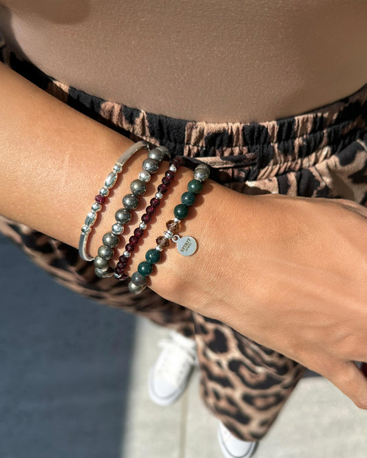 A person's wrist adorned with a bracelet and several beads, wearing leopard print pants.