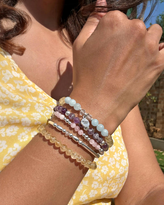 A woman wearing a yellow floral dress and multiple bracelets on her wrist.