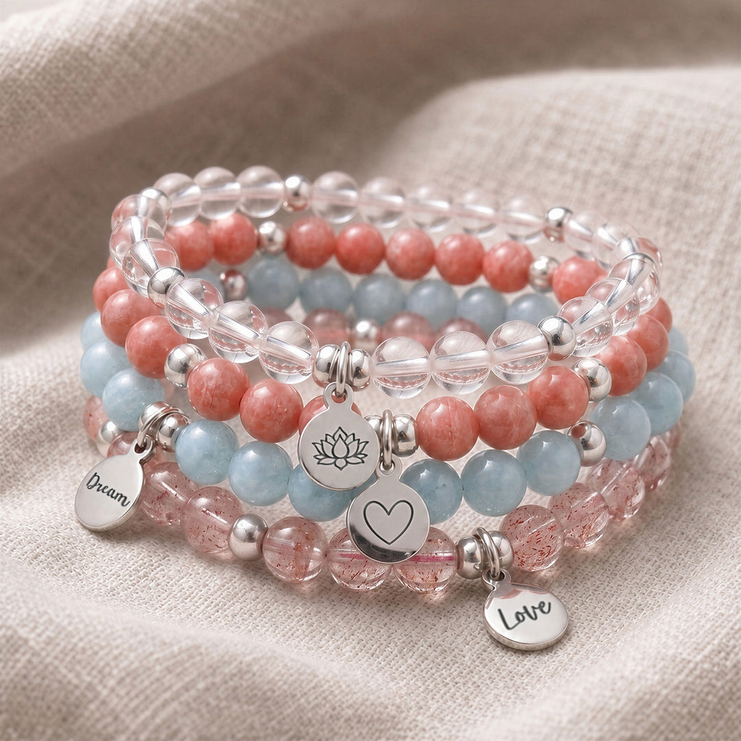 A stack of four personalised crystal gemstone bracelets — Aquamarine, Clear Quartz, Rhodochrosite, and Strawberry Quartz