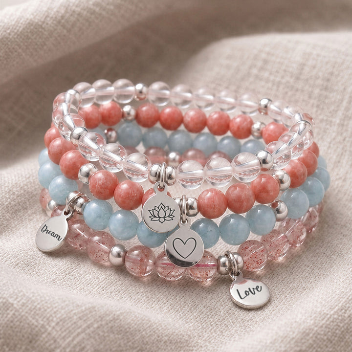 A stack of four personalised crystal gemstone bracelets — Aquamarine, Clear Quartz, Rhodochrosite, and Strawberry Quartz