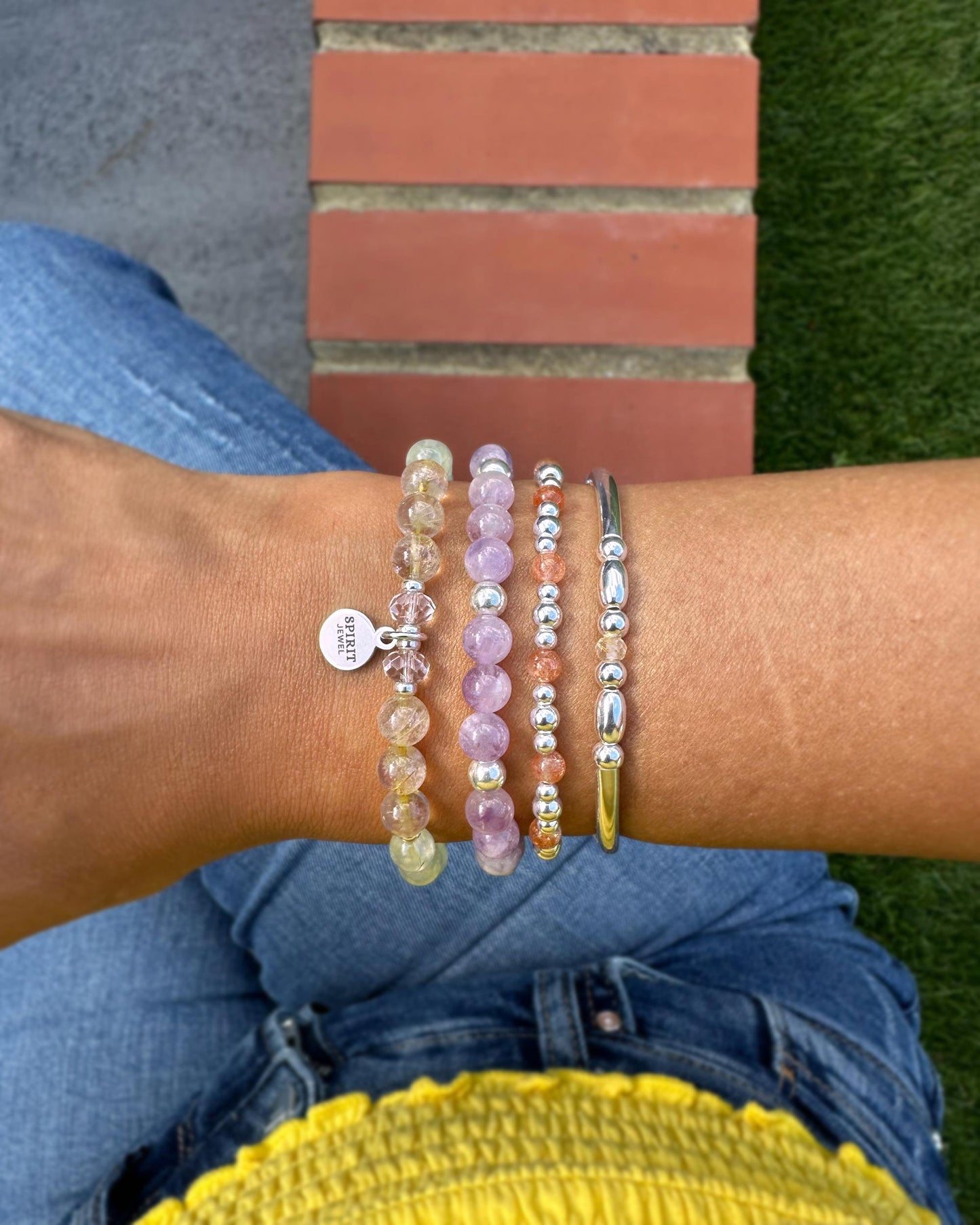A person's wrist adorned with a collection of colorful beaded bracelets, including a silver bracelet and a bracelet with a charm.