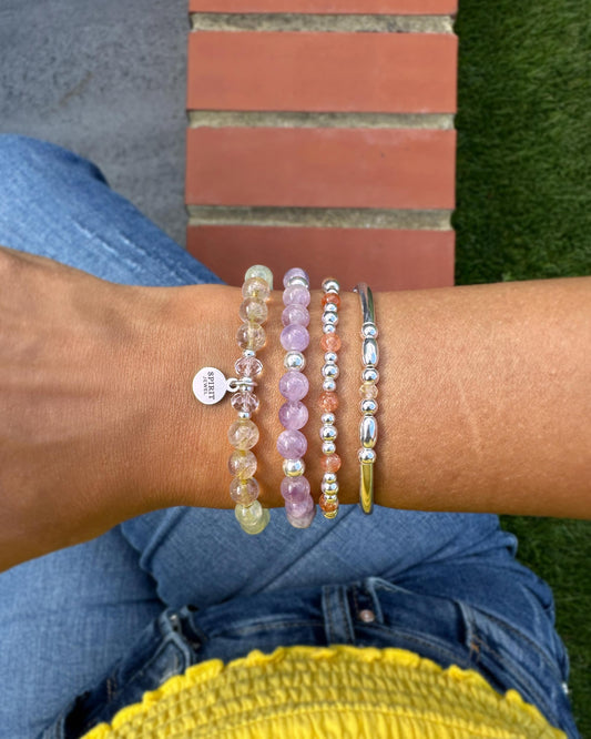 A person's wrist adorned with a collection of colorful beaded bracelets, including a silver bracelet and a bracelet with a charm.