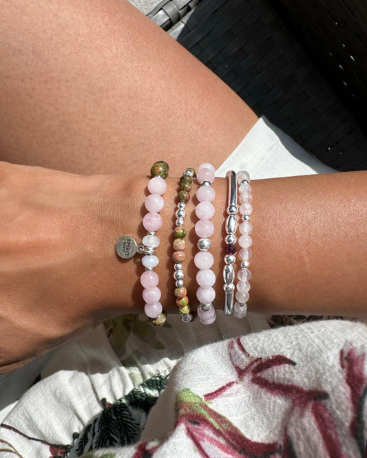A person's wrist adorned with a collection of colorful beaded bracelets, including pink, silver, and green beads, as well as a charm bracelet.