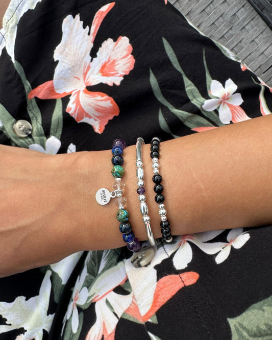 A person's wrist adorned with three bracelets, each with different colored beads and charms, set against a floral print dress.